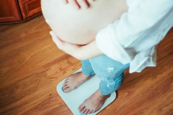 Image of woman weighing herself and experiencing weight gain through pregnancy East Malling